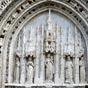 Détail du porche d'entrée de l'église Sainte Radegonde. Le portail de style gothique flamboyant est du XVe siècle, tout comme le rare parvis qui est conservé. Il s'agit d'un parvis de justice, entouré de bancs de pierre, sur lesquels siégeaient les juges ecclésiastiques, jugeant les affaires religieuses et civiles du bourg.